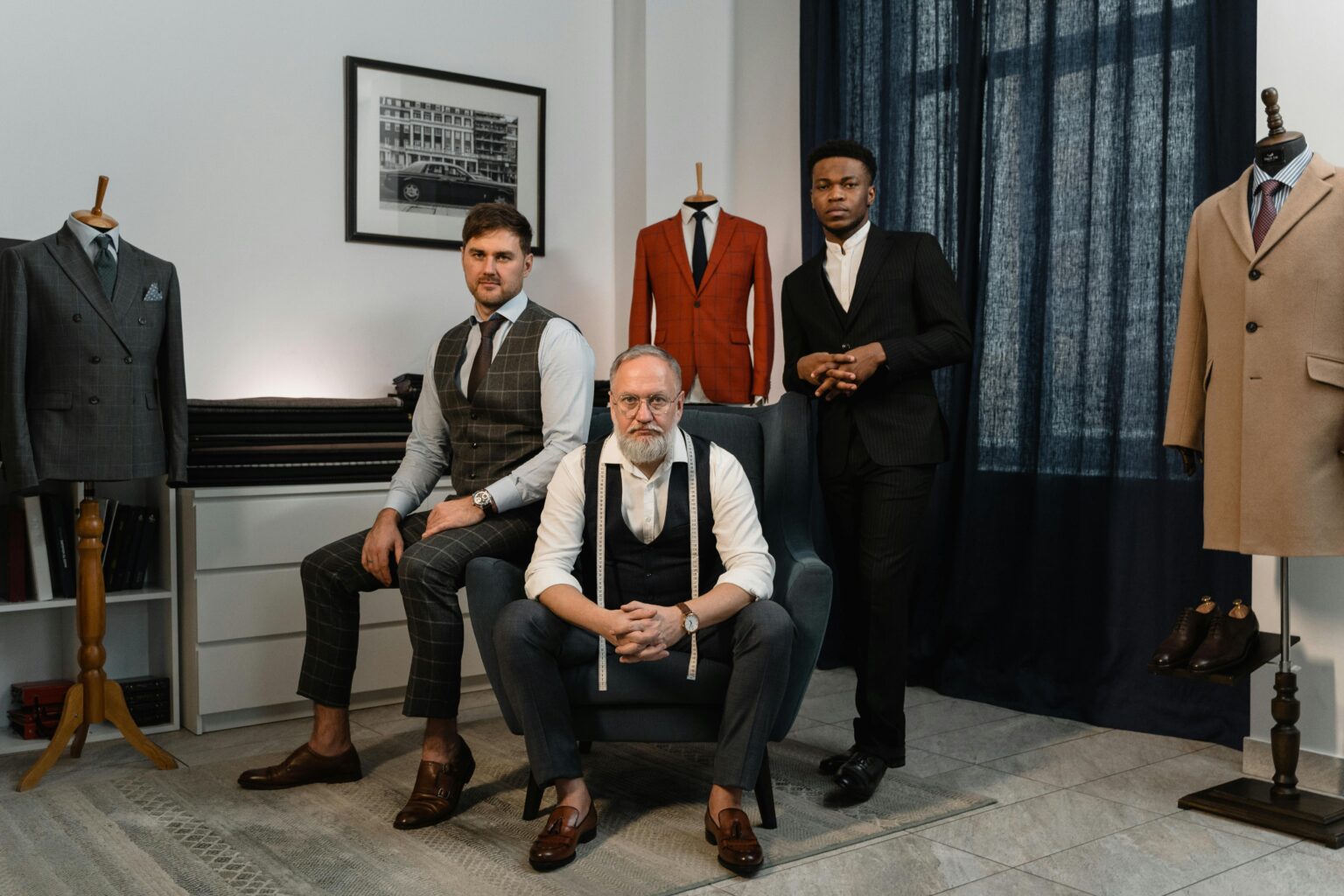 Three male fashion designers in a tailoring studio showcasing elegant suits and craftsmanship.